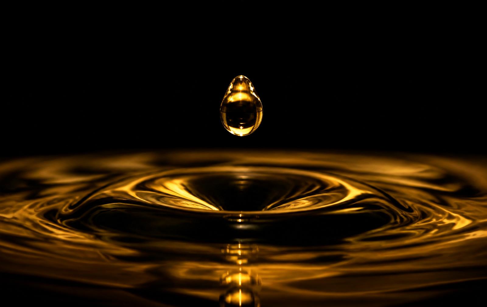 A single golden droplet suspended above a rippling amber surface